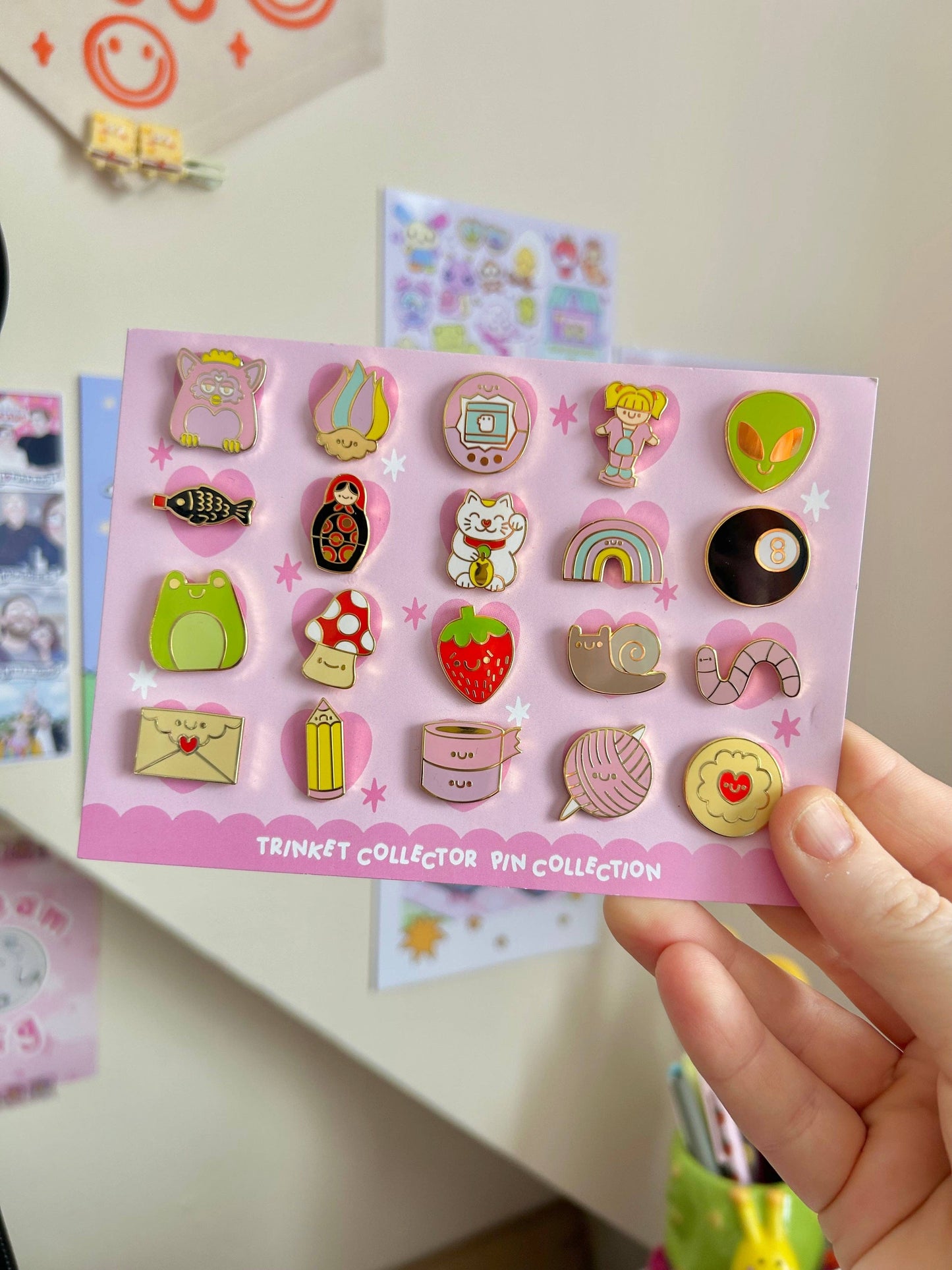 Collection of colorful pins on a pink card held by a hand with a blurred background