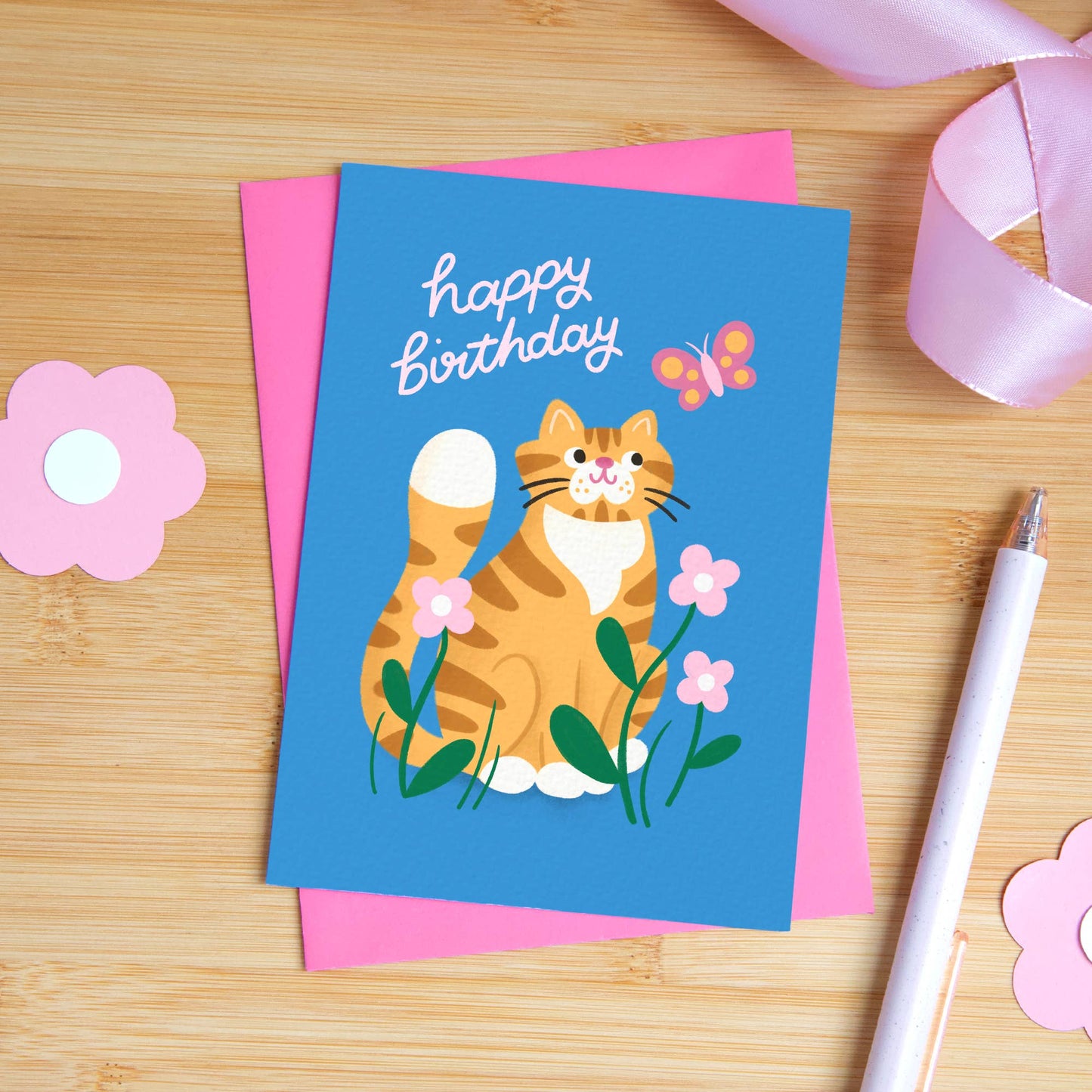 Birthday card with a cat illustration on a wooden surface with decorative items.