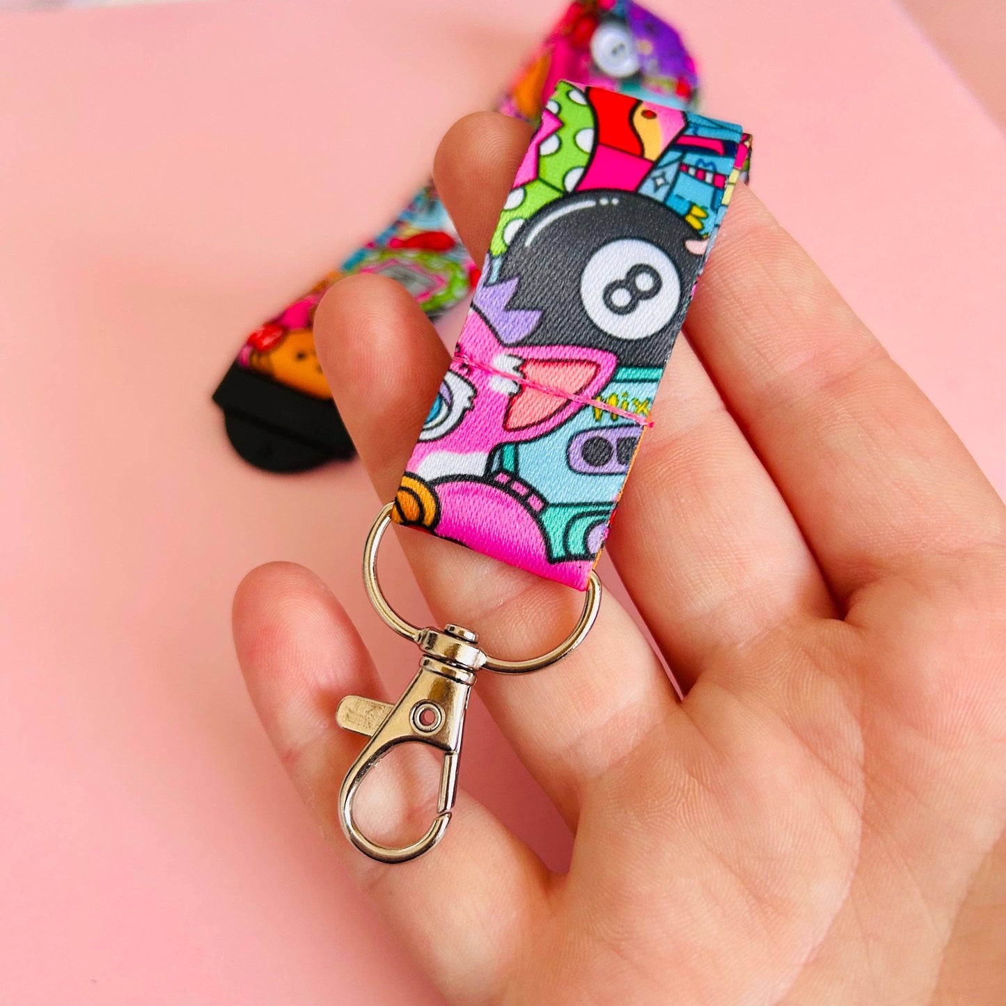 Colorful keychain with a cartoon design held by a hand against a pink background