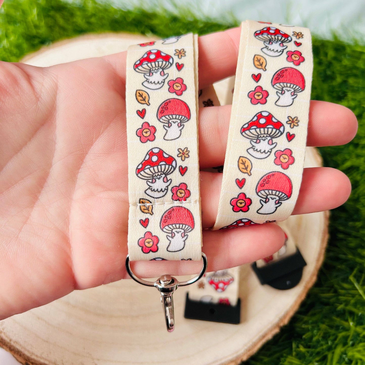 Two mushroom-patterned lanyards held in a hand with a green grass background