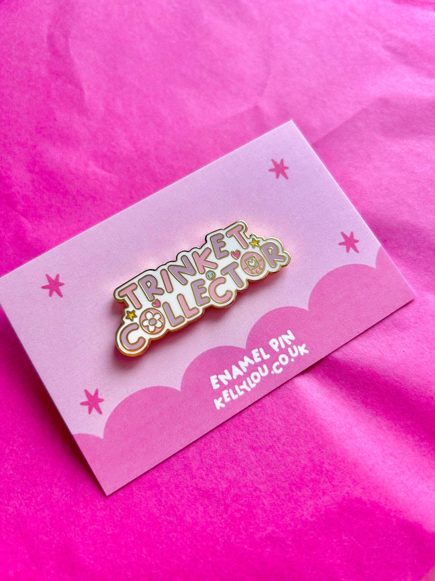 Enamel pin labeled 'Trinket Collector' on a pink card with a pink background