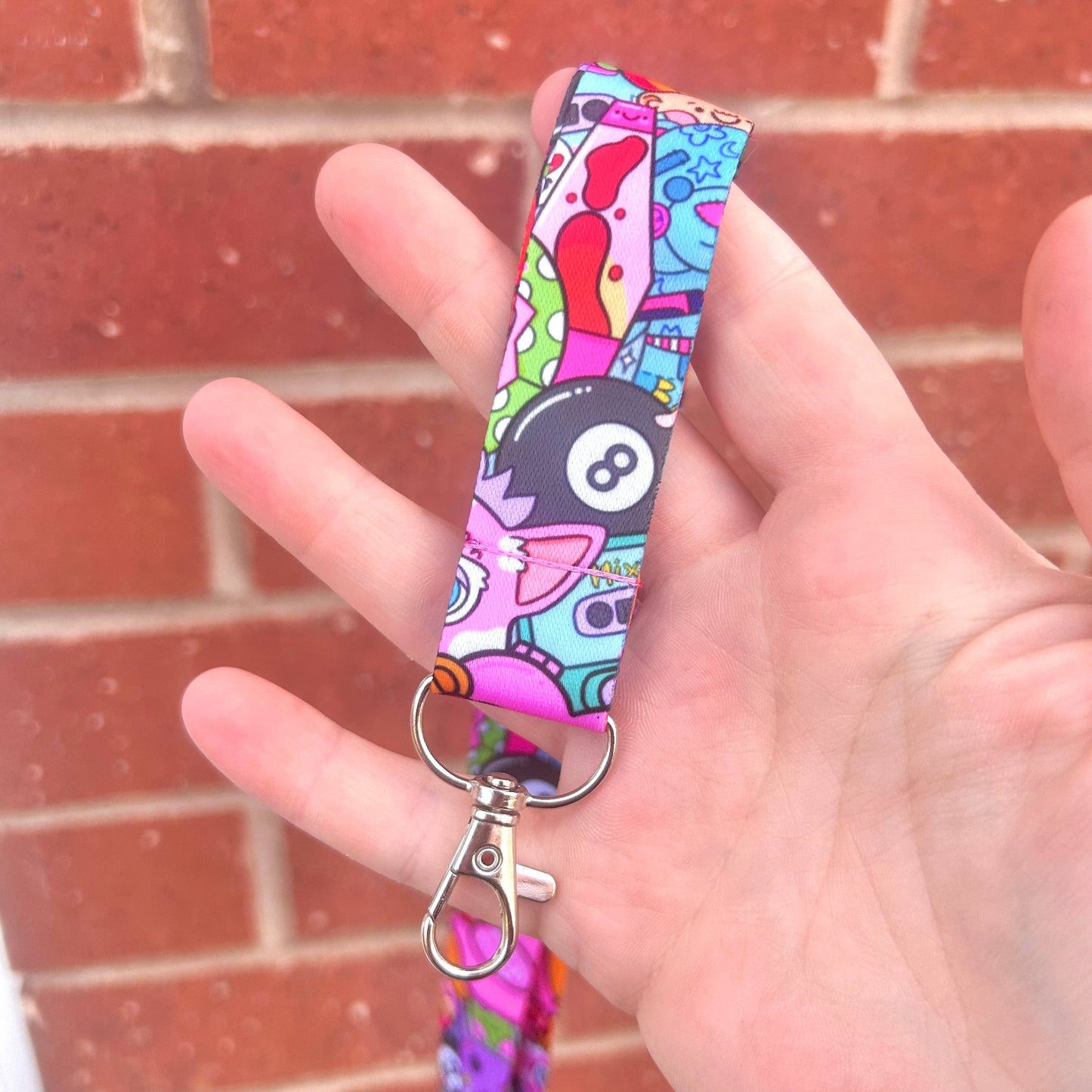 Colorful keychain with cartoon design held by a hand against a brick wall.