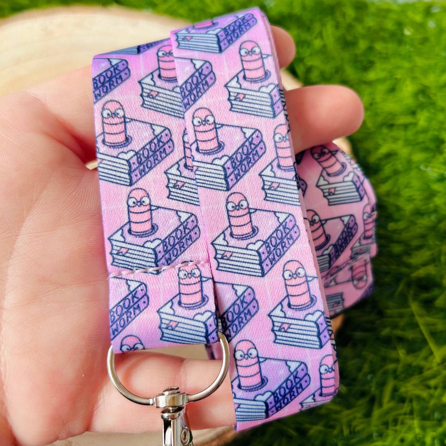 Pink keychain with cartoon design held by a hand on grass