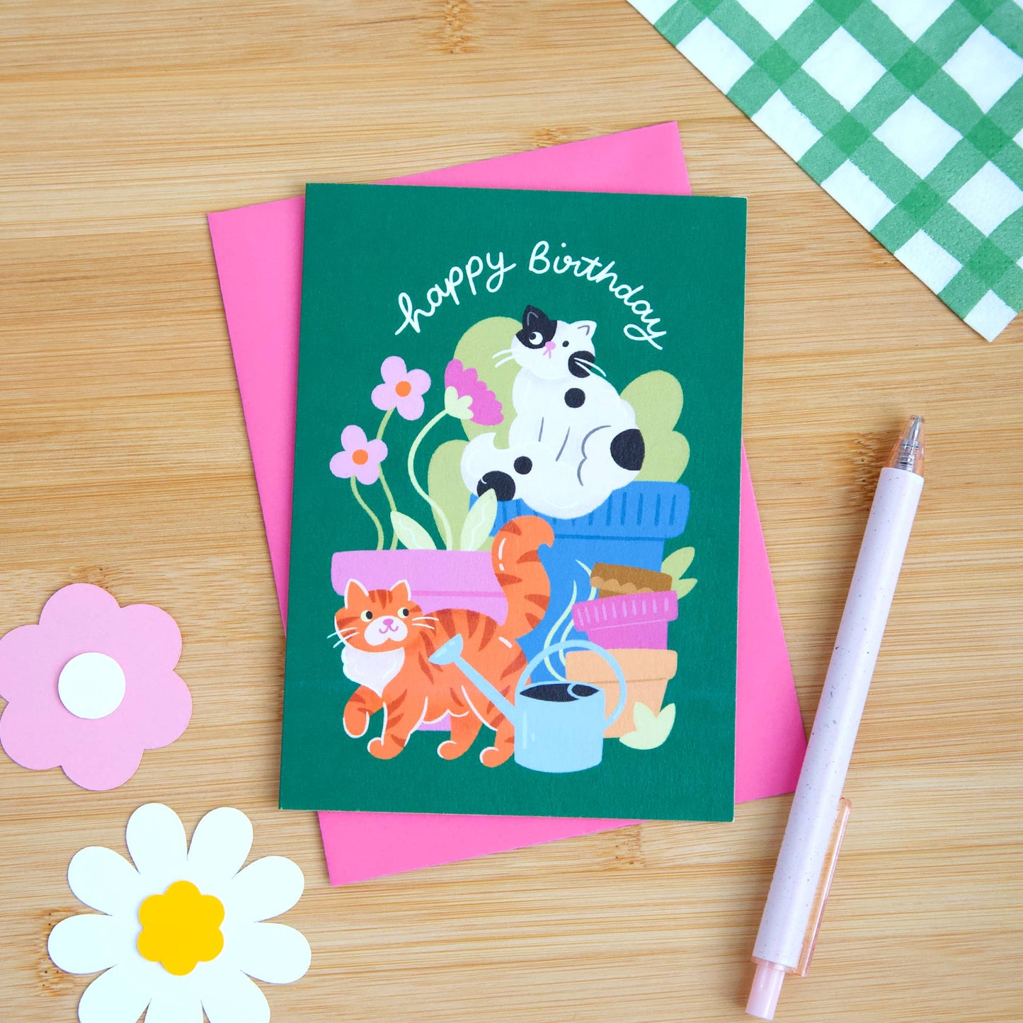 Birthday card with cats and flowers on a wooden surface with stationery items.