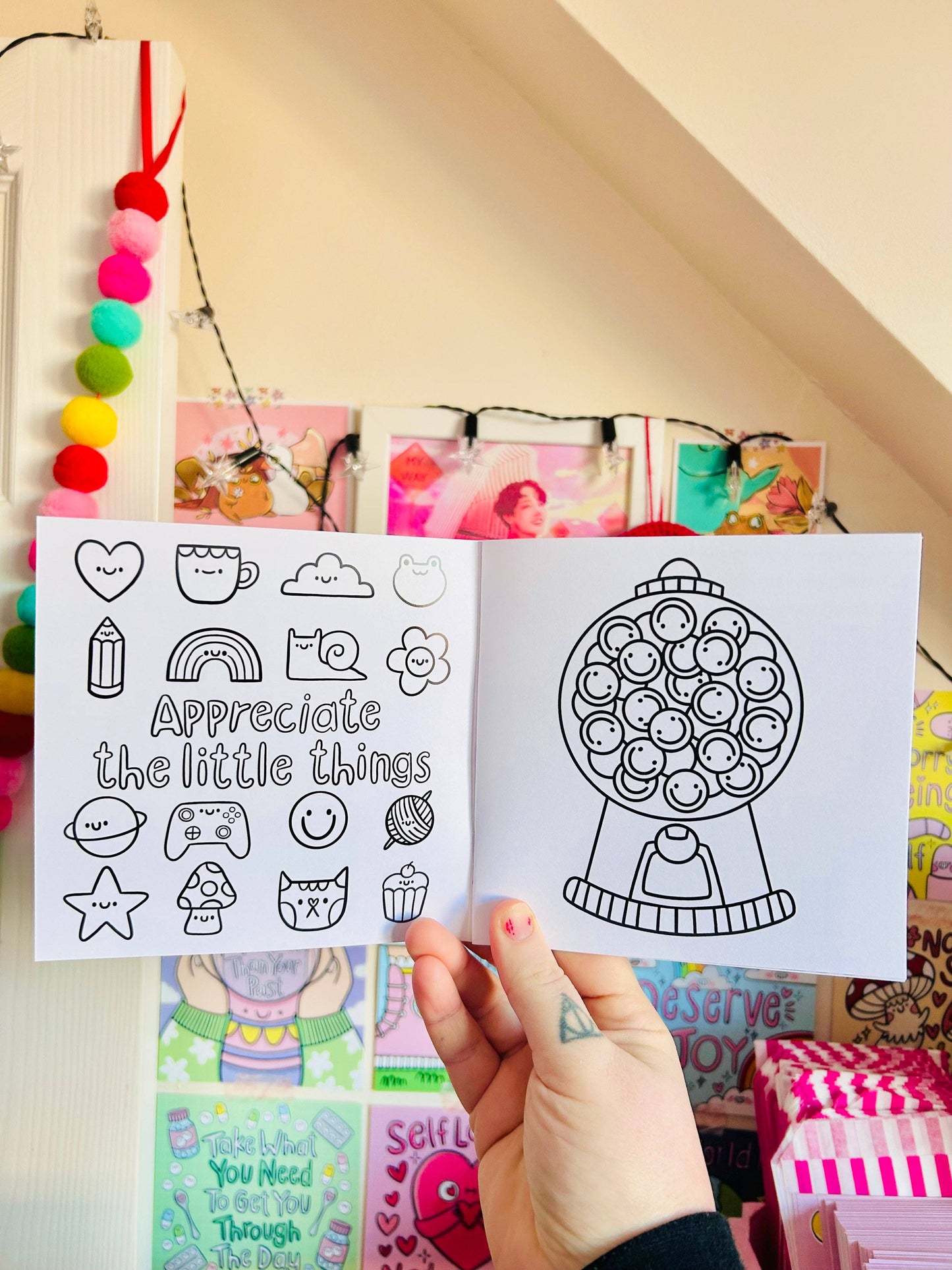 Hand holding a coloring book with black line art designs against a colorful background.