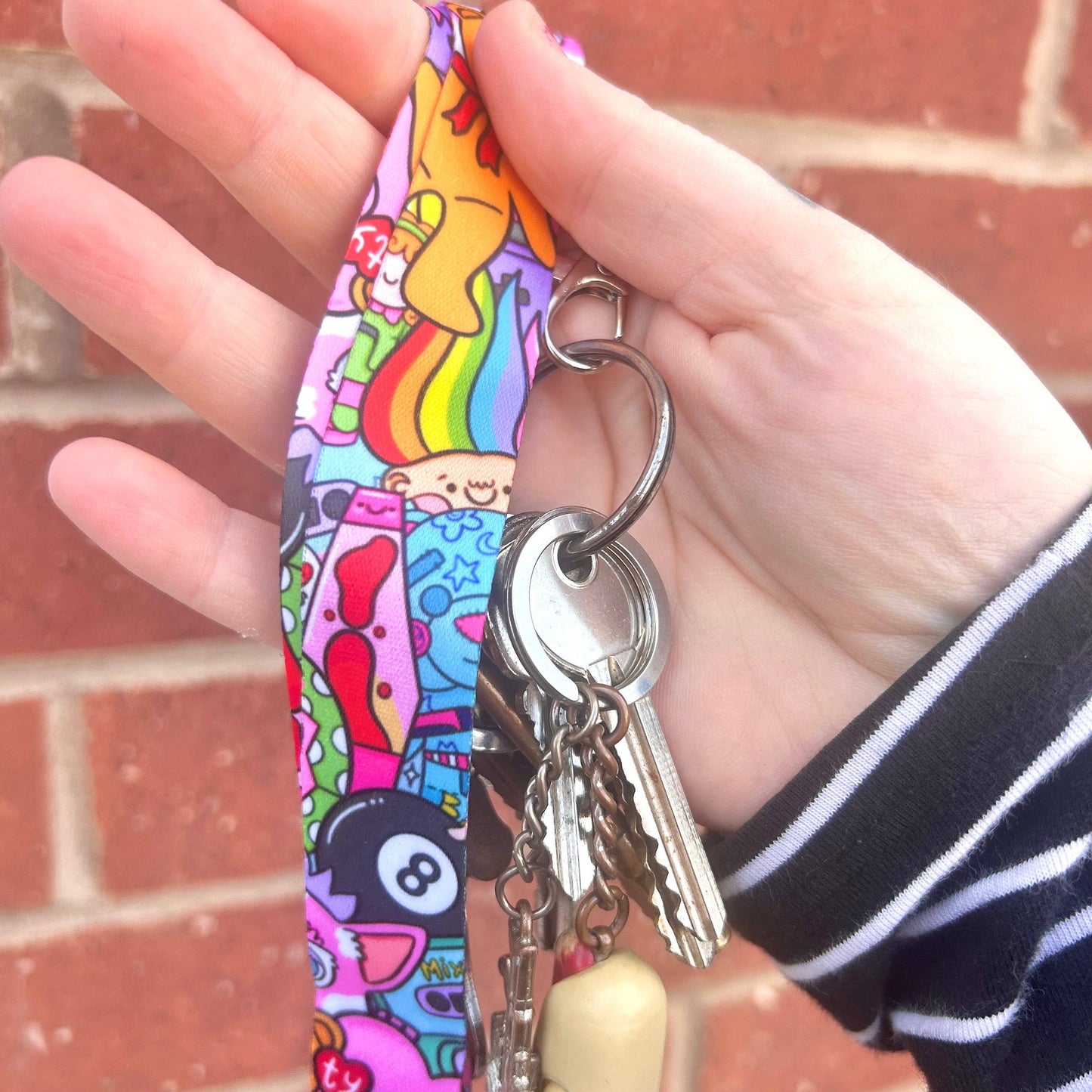 Hand holding a colorful keychain with keys against a brick wall background