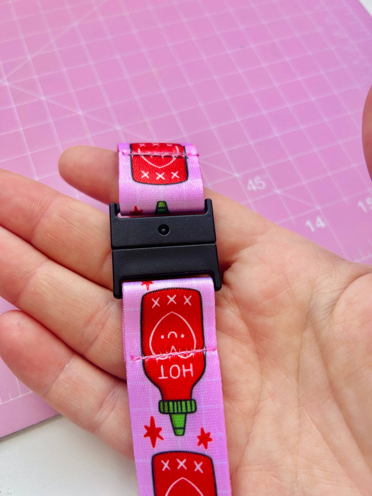 Pink dog collar with cartoon ketchup bottle design held by a hand on a pink grid background