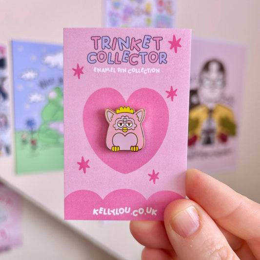 Pink enamel pin with cartoon character on a 'Trinket Collector' card held by a hand.