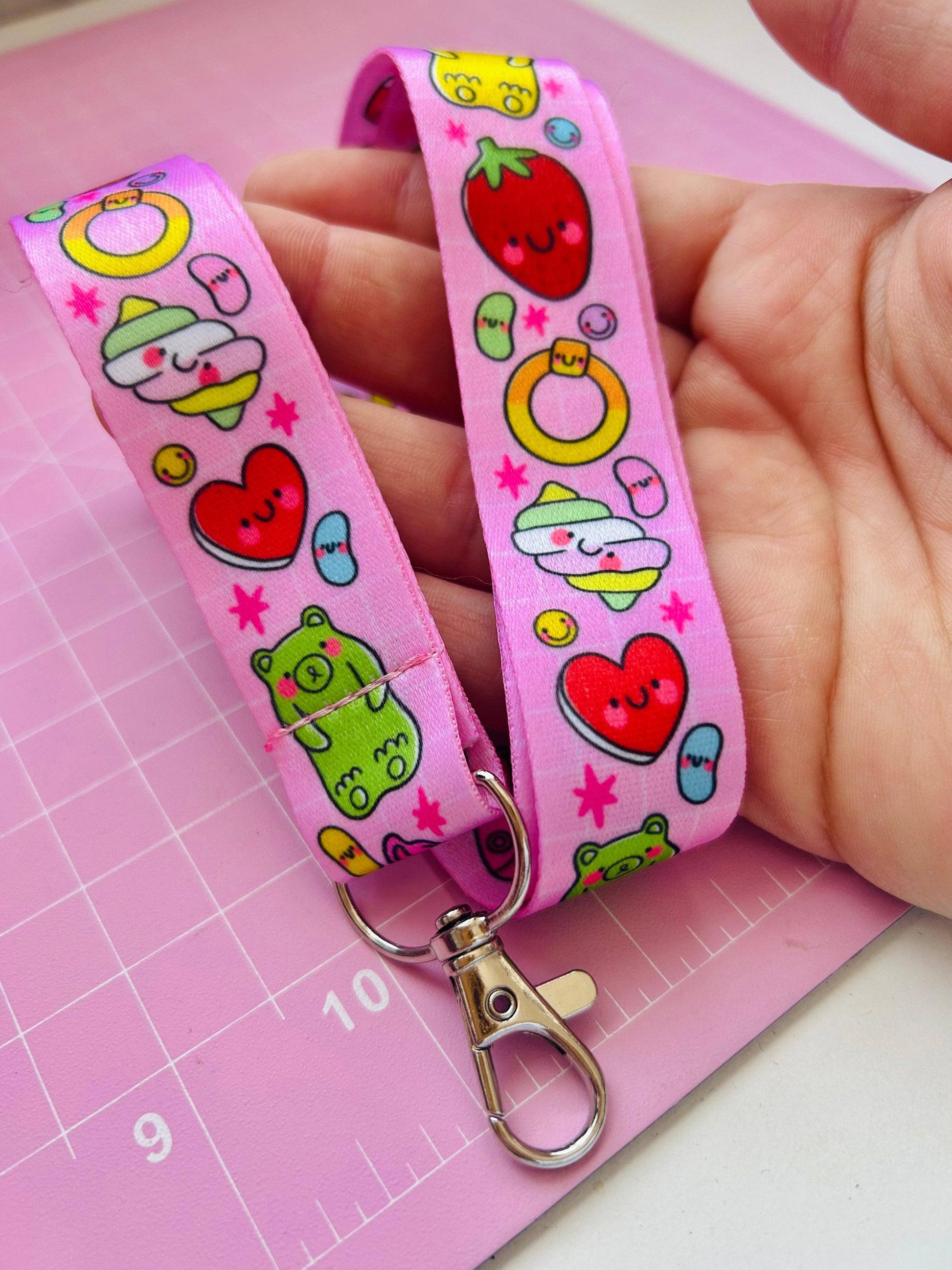 Pink lanyard with colorful cartoon designs held by a hand on a pink cutting mat.
