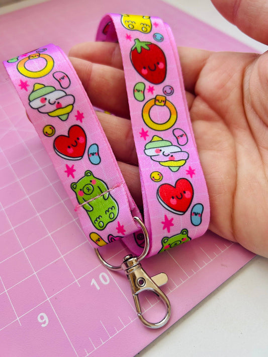 Pink lanyard with colorful cartoon designs held by a hand on a pink cutting mat.
