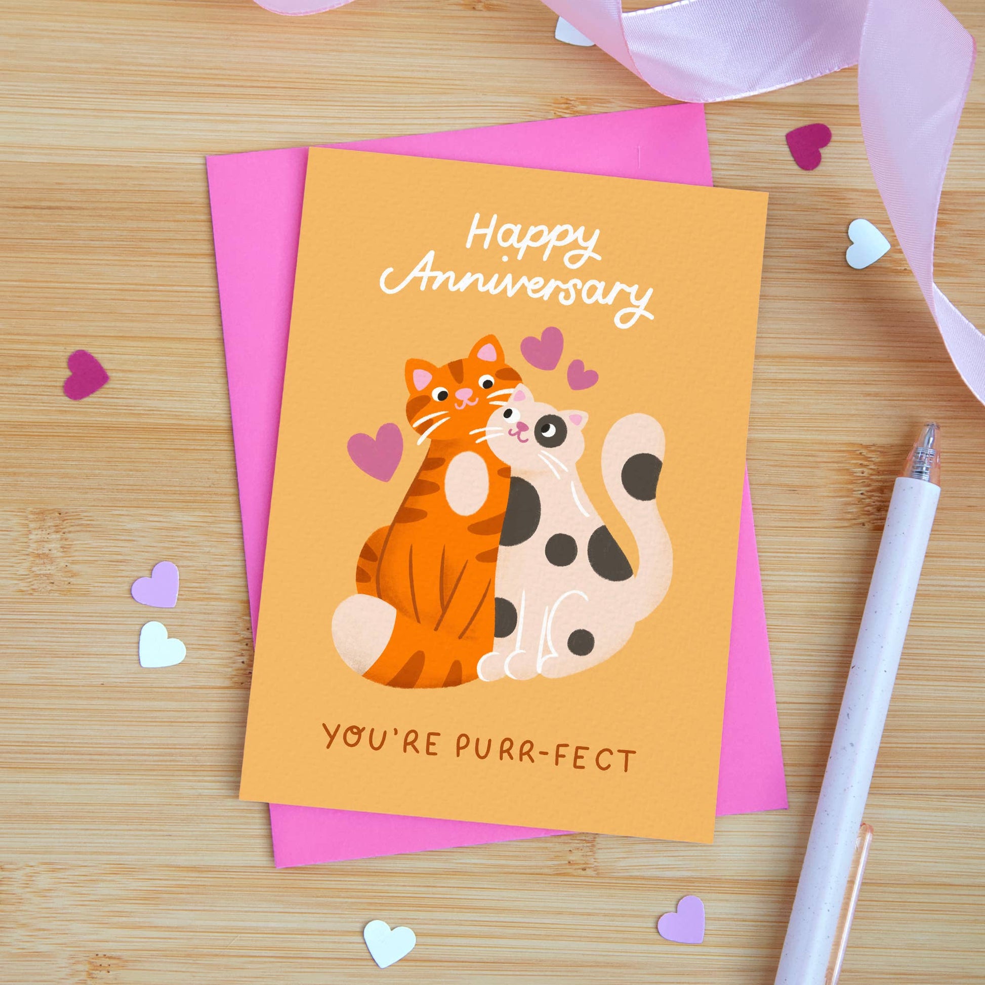Anniversary card with cats and hearts on a wooden surface