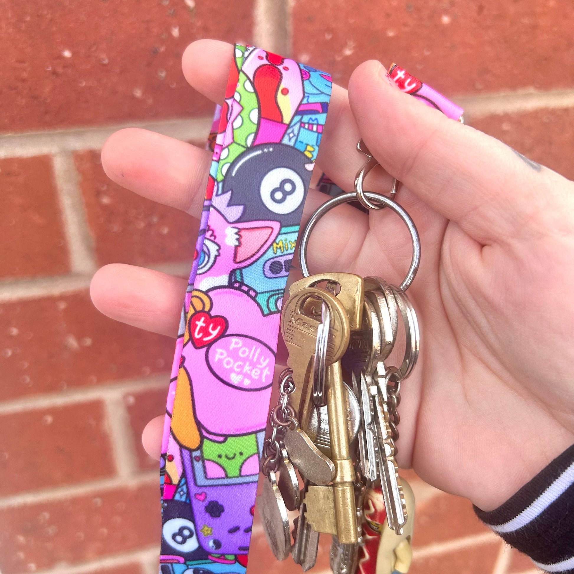 Hand holding a colorful keychain with keys against a brick wall background
