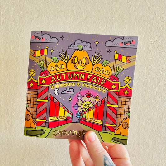 Coloring book with 'Autumn Fair' design held against a beige wall