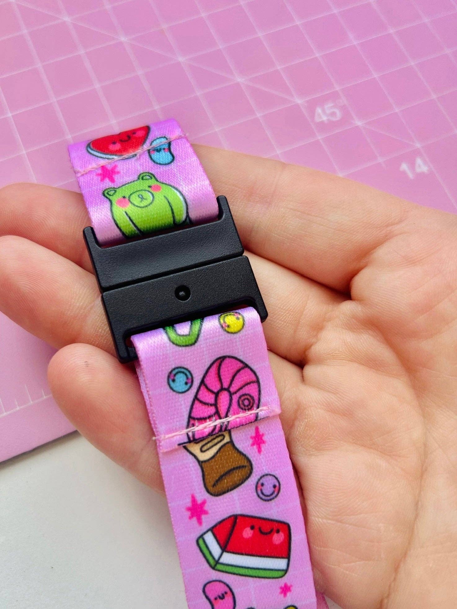 Hand holding a colorful belt with cartoon designs on a pink grid background