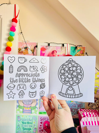 Hand holding a coloring book with black line art designs against a colorful background.