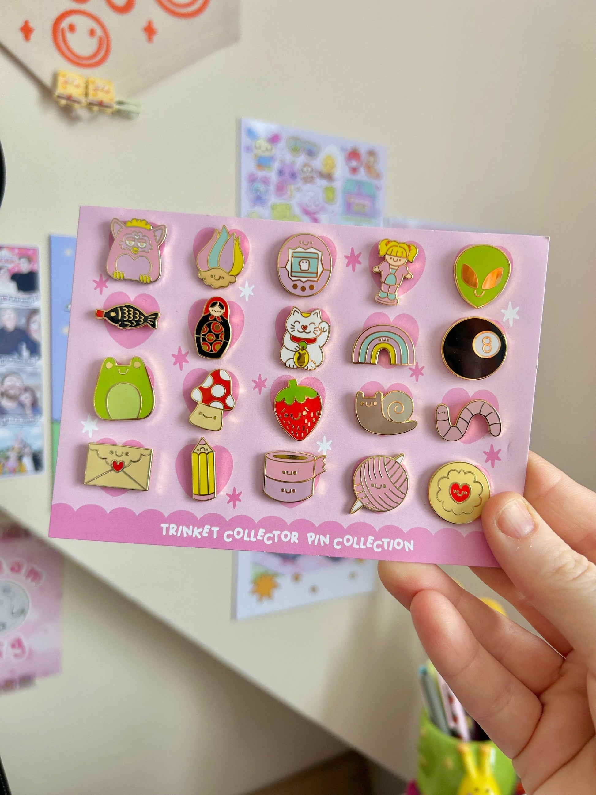Collection of colorful pins on a pink card held by a hand against a light background.
