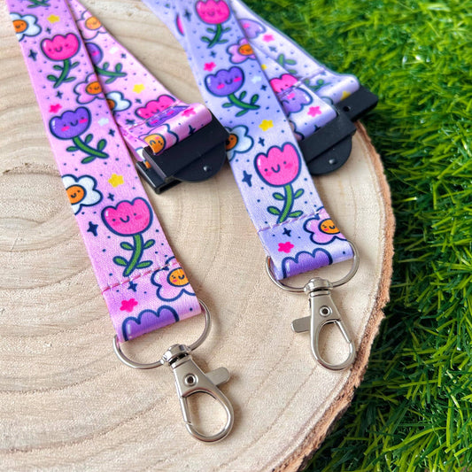 Floral patterned lanyard with keychain on a wooden surface with grass in the background