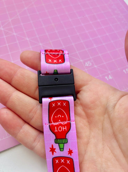 Pink dog collar with cartoon ketchup bottle design held by a hand on a pink grid background