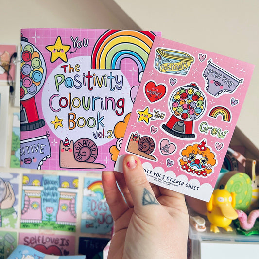 Positivity Colouring Book Vol.2 and Sticker Sheet held by a hand with visible tattoos.