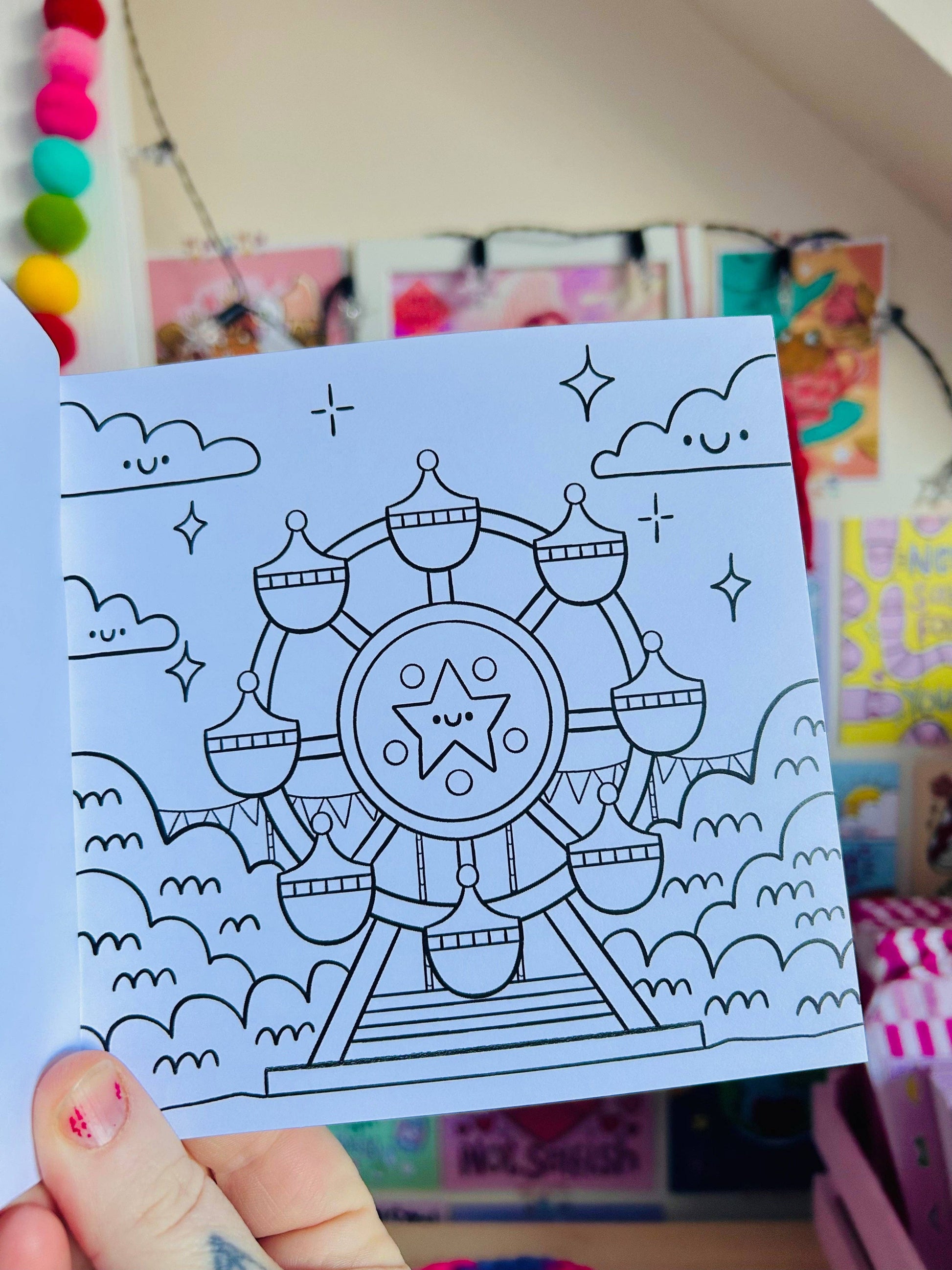 Coloring book with a ferris wheel design held by a hand against a colorful background.